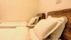Two single beds with white linens and pillows, a wooden headboard, and a wall-mounted light switch. - Hotel XYZ (Guwahati)