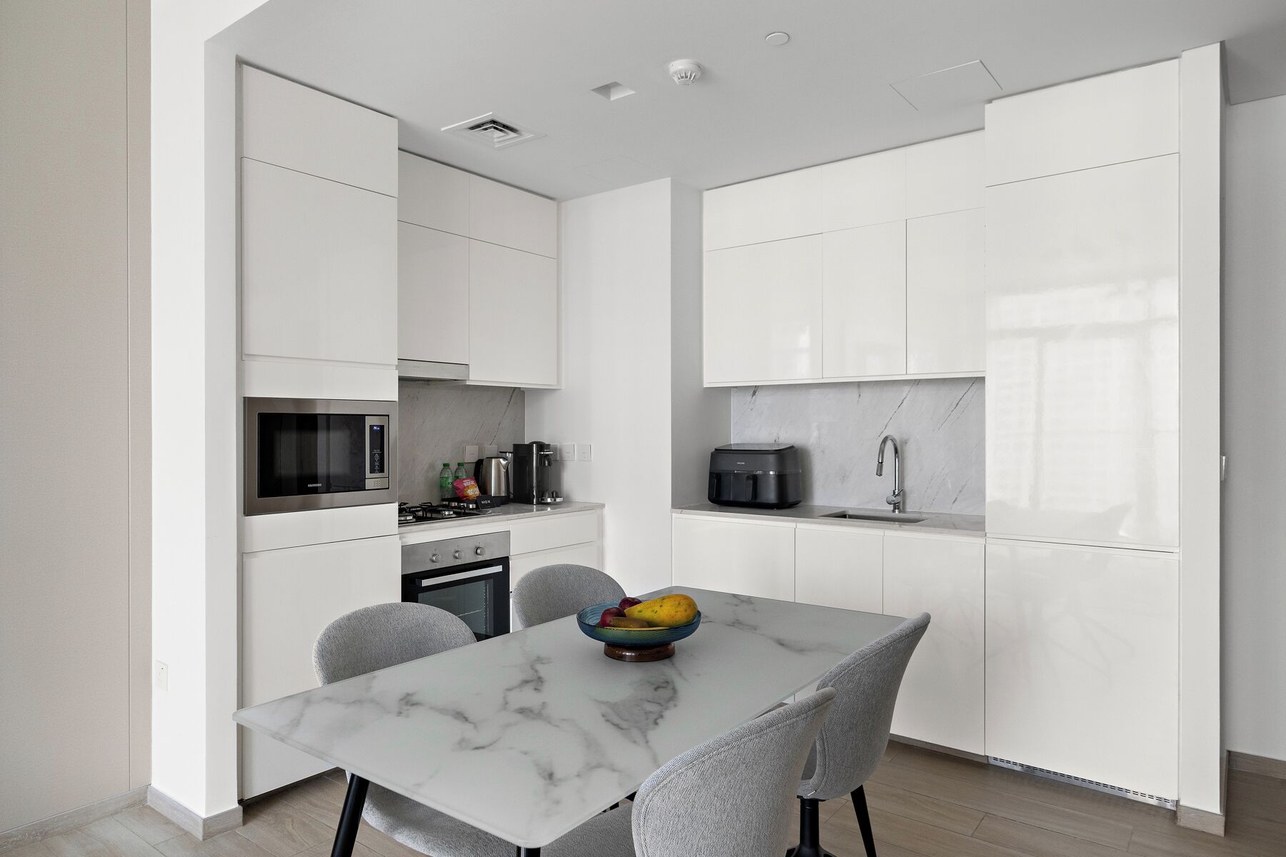 A modern kitchen with white cabinetry, a marble countertop, and a dining area with a table and chairs.