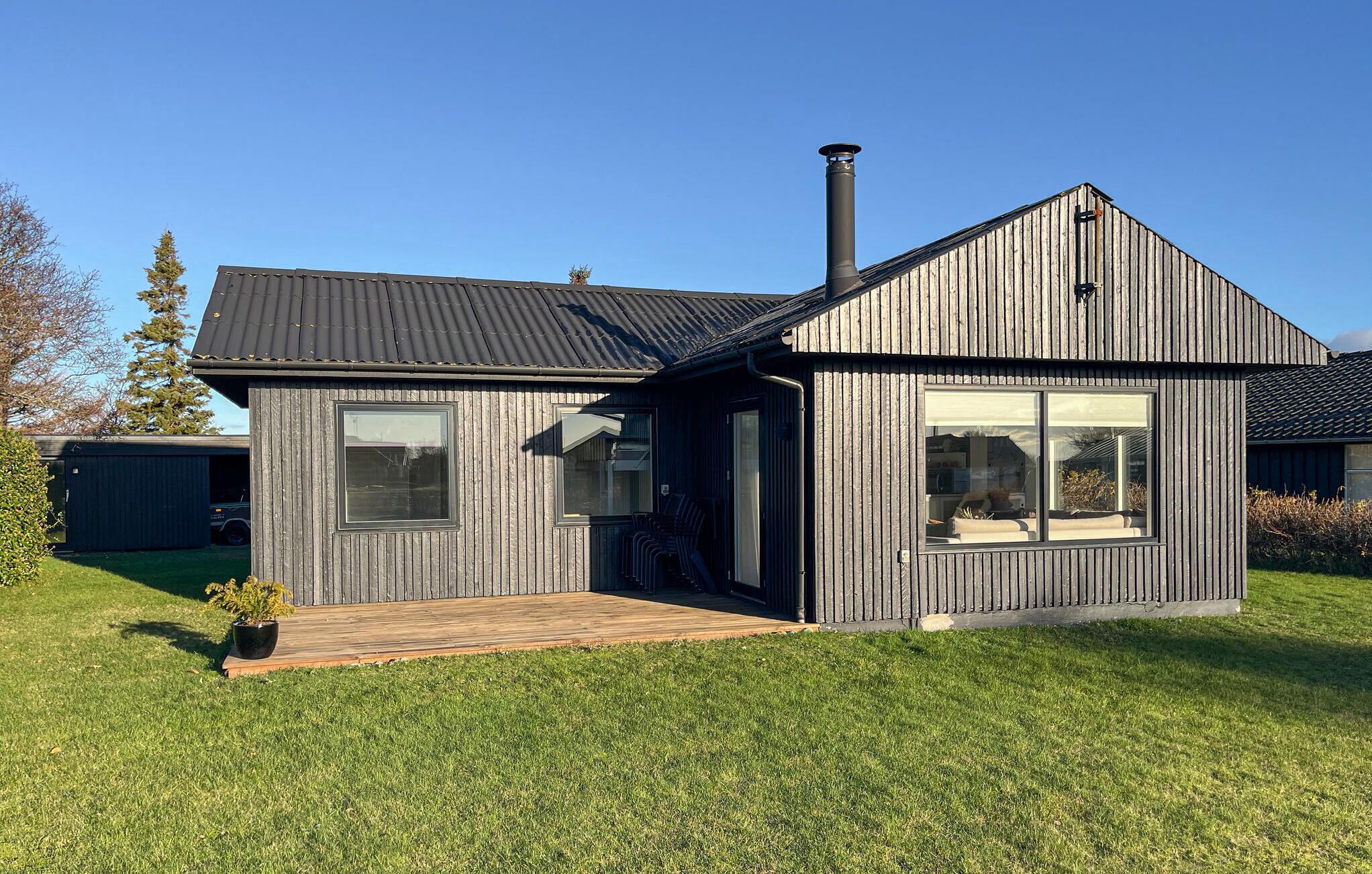 A modern house with a dark wooden exterior, a chimney, and a large window.