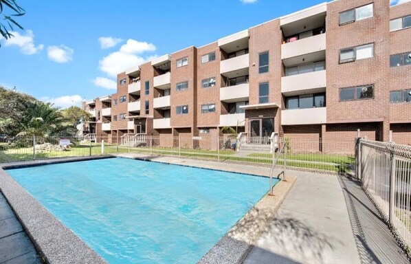 A multi-story apartment building with a swimming pool in front.