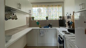 A compact kitchen with white cabinets, a sink, a stove, and a window with floral curtains.