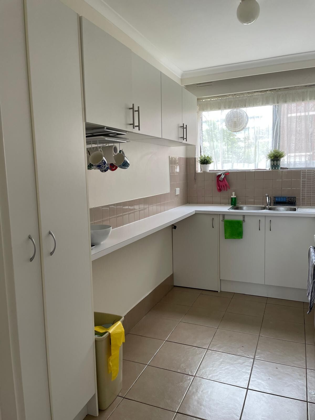 Een keuken met witte kastjes, een raam met gordijn en een spoelbak.