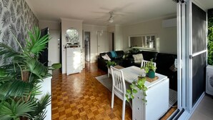 Una sala de estar moderna con suelo de madera, un sofá negro, una mesa blanca y un ventanal corredero que da a un balcón.
