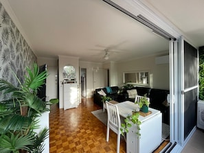 Ein modernes Wohnzimmer mit Holzboden, einer schwarzen Couch, einem weißen Tisch und einer Glasschiebetür, die auf einen Balkon führt.