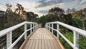 A wooden bridge with white railings, surrounded by dense greenery and trees.