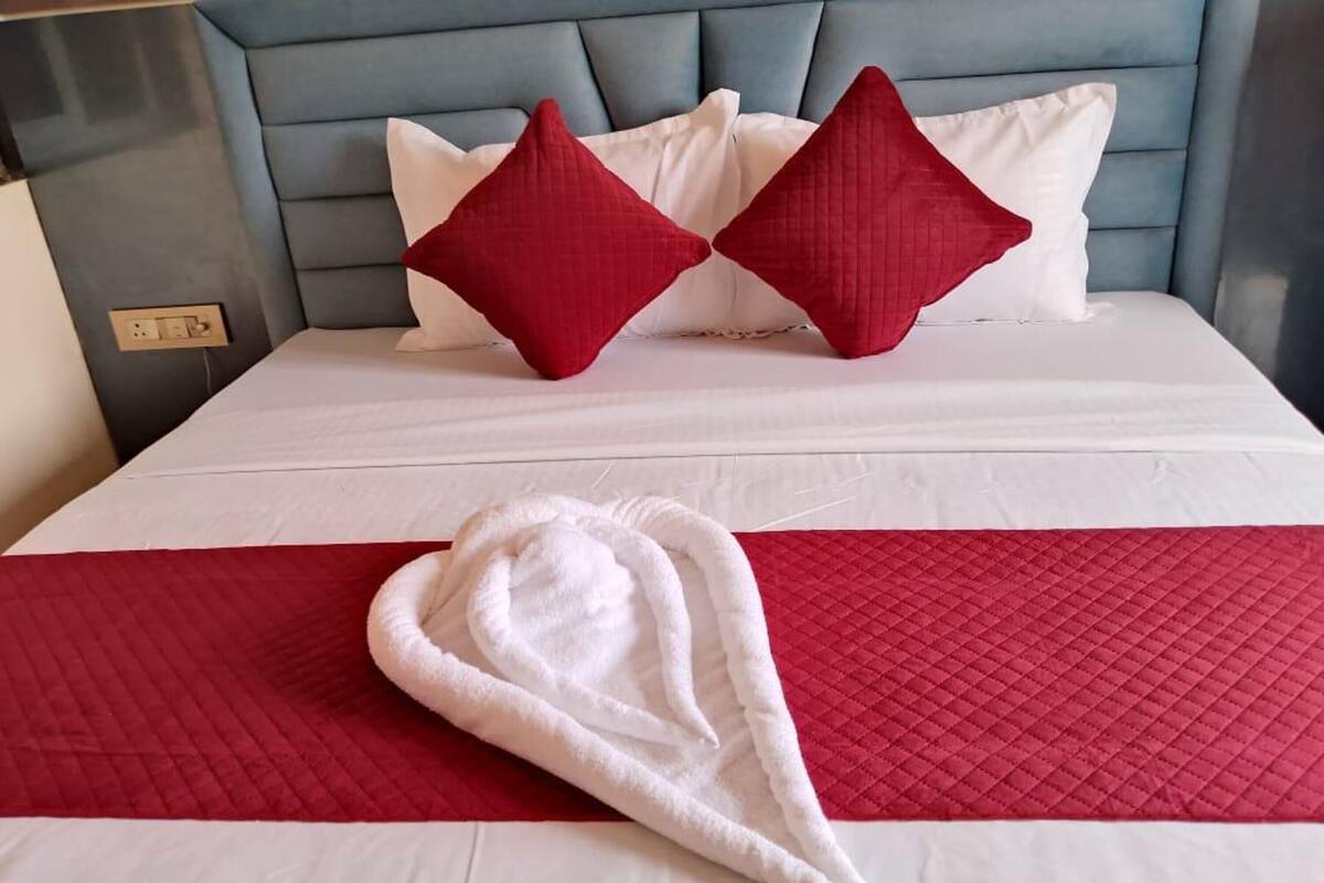 A neatly made bed with a white and red bedspread, two red pillows, and a white towel on the bed.