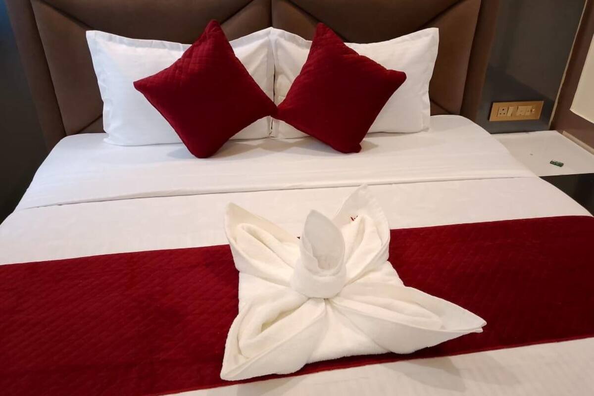Ein ordentlich bezogenes Bett mit weißen Bettwäsche, zwei roten Kissen und einer roten Bettdecke mit weißen Streifen.