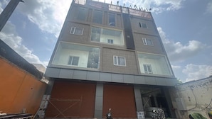 A multi-story building with a closed garage door, a metal fence, and construction materials visible on the ground. - Hotel Kamla Kishan (Khatoo)