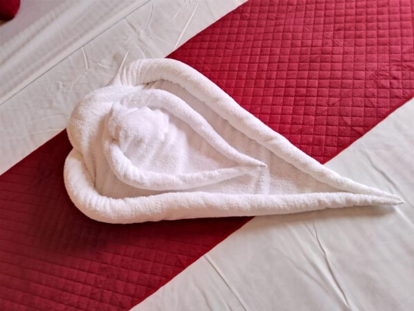 A white towel on a bed with a red and white quilted bedspread. - Hotel Kamla Kishan (Khatoo)