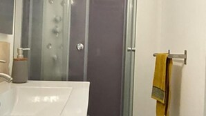 Une salle de bain avec une douche à parois de verre, un lavabo blanc et un porte-serviettes sur lequel est posée une serviette jaune.