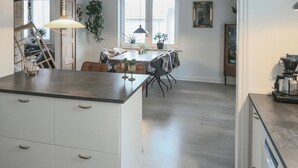Una cocina con una isla central, un comedor con mesa y sillas, y una escalera que lleva a otro nivel.