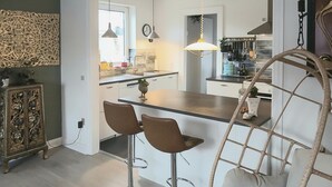 Una cocina moderna con una isla central, dos taburetes de bar, una lámpara colgante y un mueble decorativo.