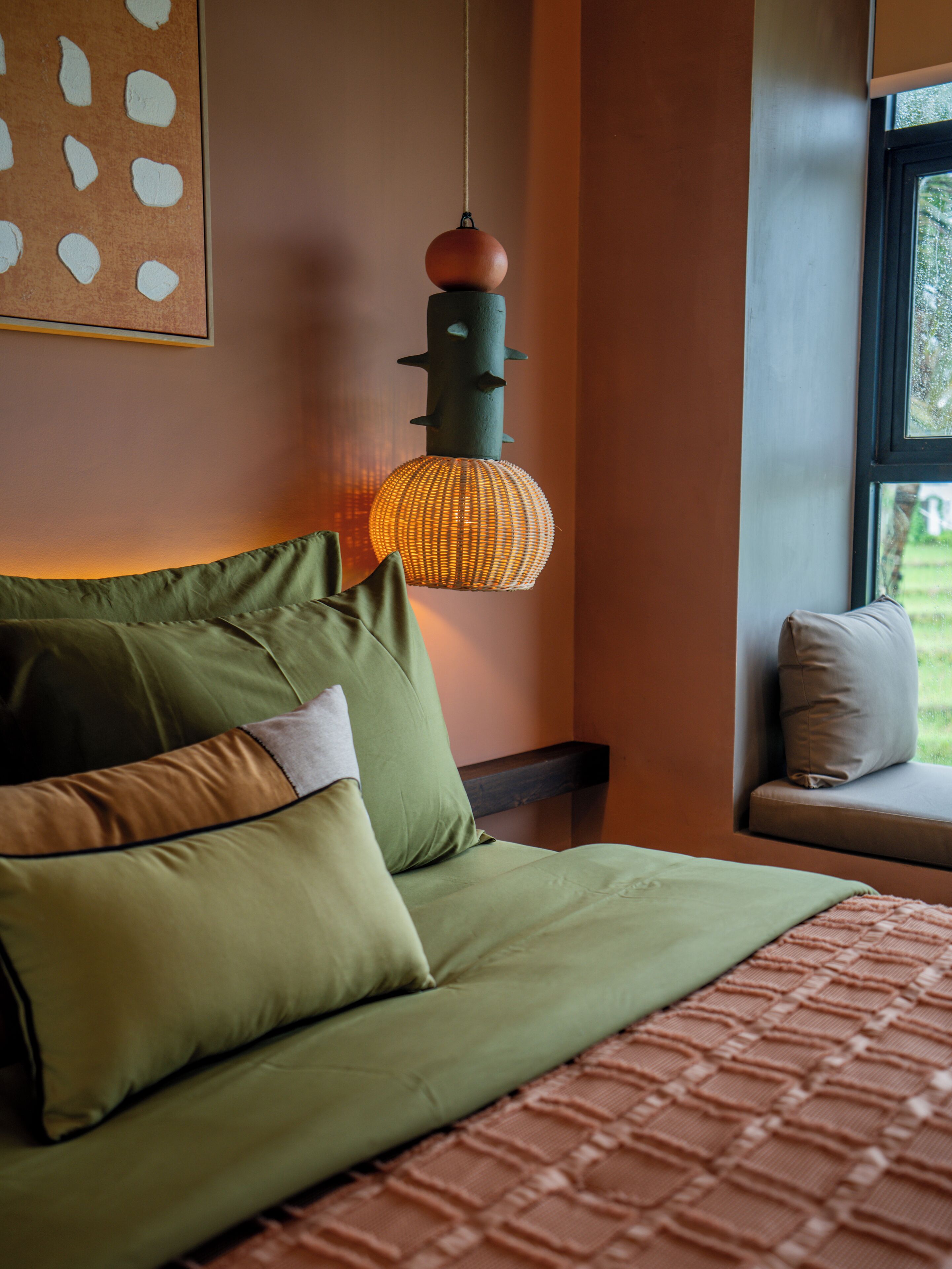 A bed with green bedding, a hanging light fixture, and a window with a view of greenery.