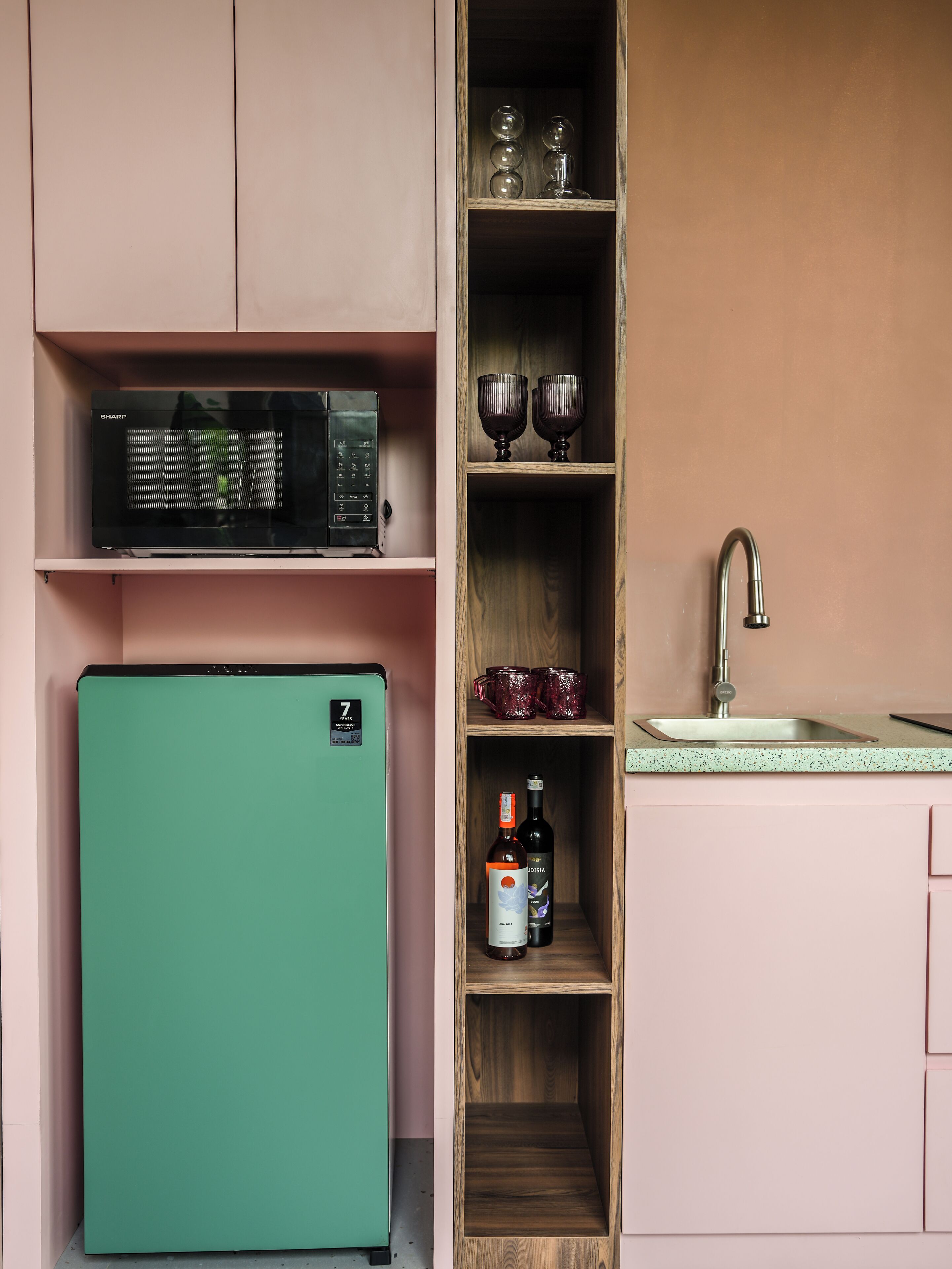 Eine kleine Küche mit einem grünen Kühlschrank, einer Mikrowelle, einem Spülbecken und Regalen mit Gläsern und Flaschen.
