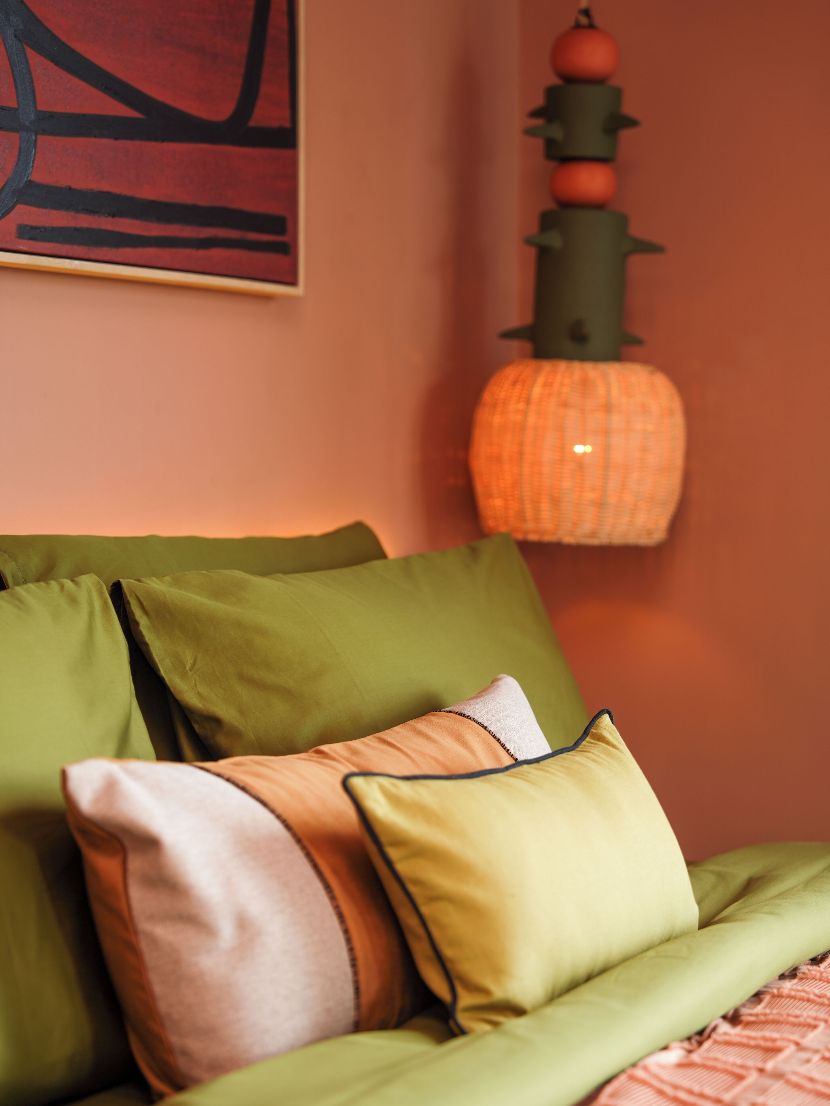 A bed with green bedding and multiple pillows, a wall with a pumpkin decoration, and a piece of abstract art.