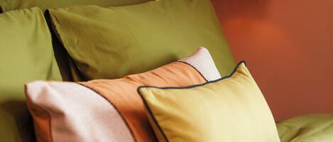A bed with green bedding and multiple pillows, a wall with a pumpkin decoration, and a piece of abstract art.
