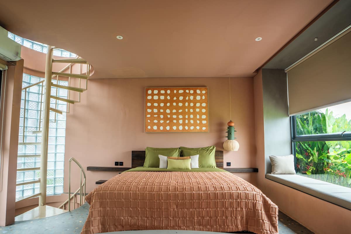 Une chambre à coucher avec un lit, une fenêtre donnant sur un paysage verdoyant, une œuvre d’art accrochée au mur et un escalier.