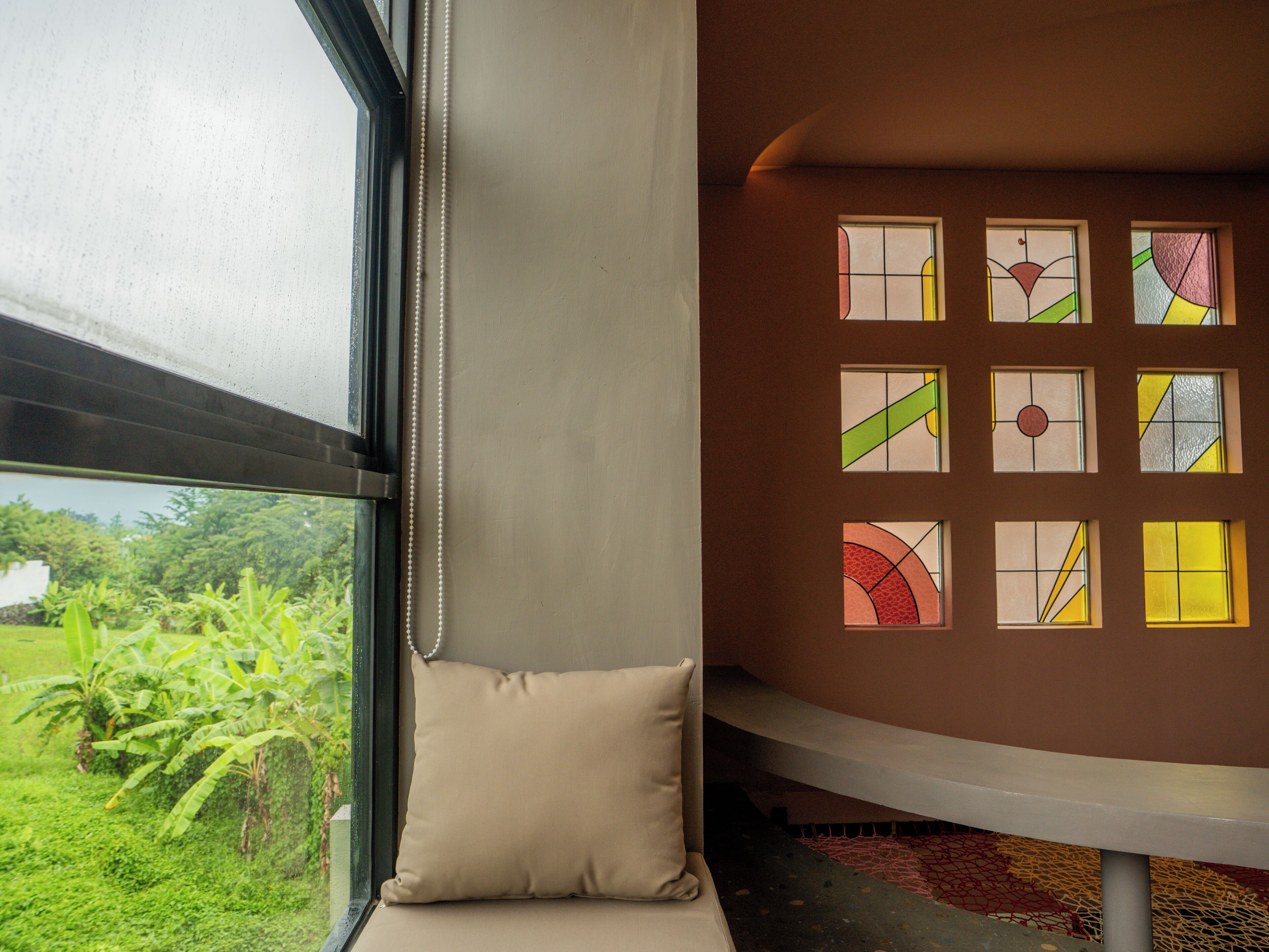 A room with a large window, a beige cushion, and a wall with colorful stained glass windows.