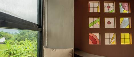 A room with a large window, a beige cushion, and a wall with colorful stained glass windows.