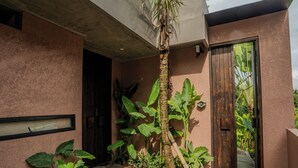 A modern building with a concrete facade, a wooden door, and a concrete pathway leading to the entrance. - Patha (Canggu)