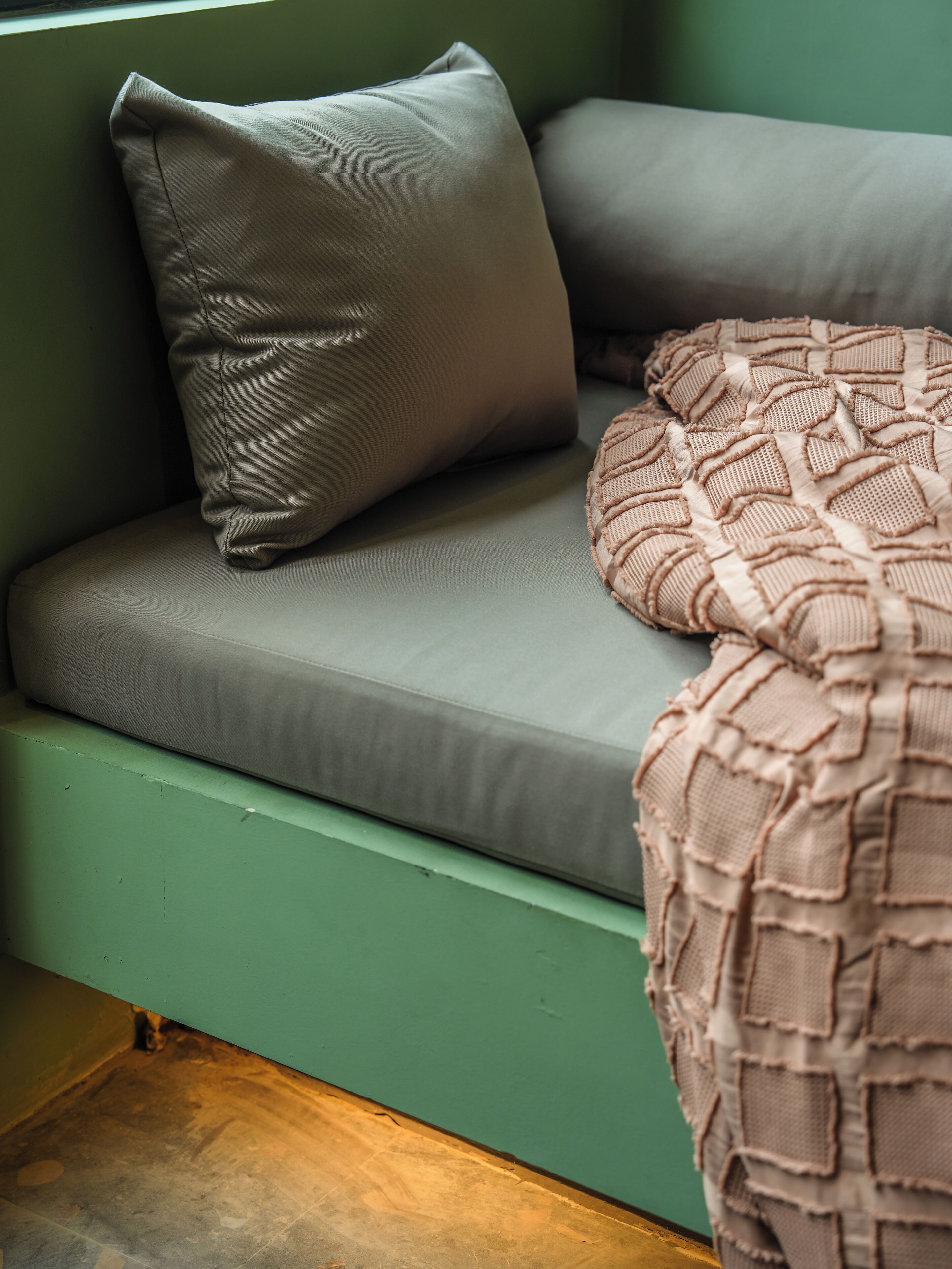 A green sofa with a grey cushion and a textured blanket.