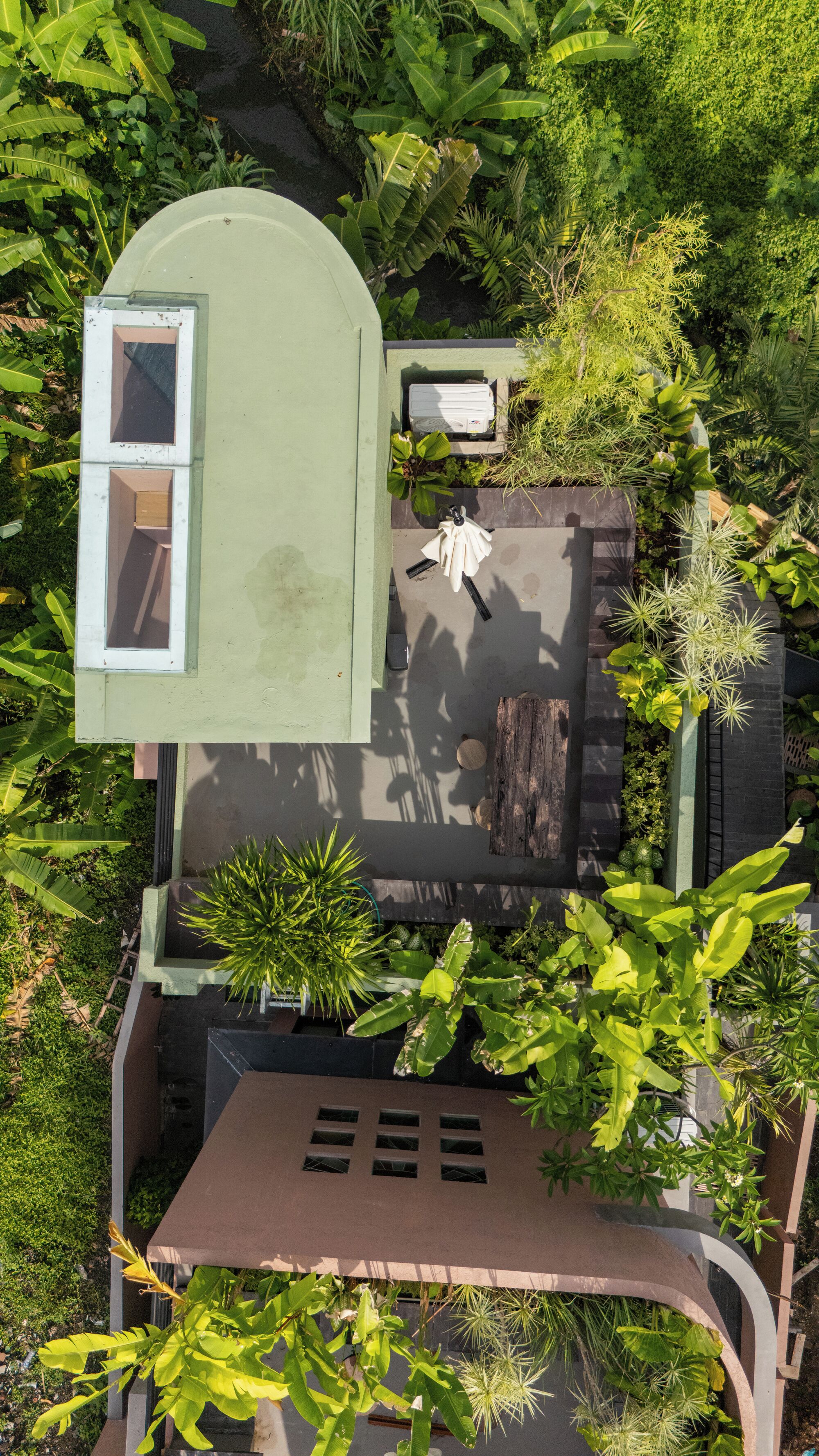 An aerial view of a modern house with a green roof, a small enclosed porch, and a garden with various plants.