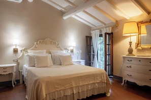 Un dormitorio con una cama grande, dos mesitas de noche, un tocador, un espejo y una ventana con cortinas.