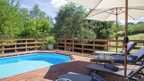Una terraza de madera con piscina, sillas de descanso y una sombrilla.