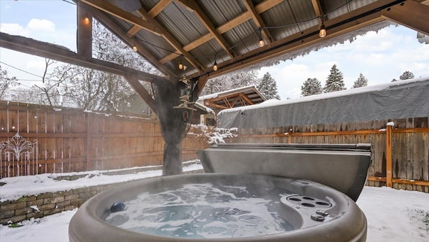 Un jacuzzi bajo un porche cubierto, con un cerco de madera y nieve en el suelo.