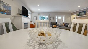 Una sala de estar moderna con una mesa redonda blanca en primer plano, una chimenea, un sofá y un televisor.