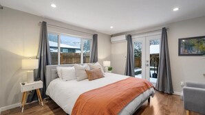 Un dormitorio moderno con una cama grande, una mesita de noche, una lámpara y vistas al exterior a través de un ventanal.