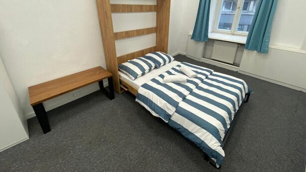 A bedroom with a wooden bed frame, a bench, and a window with curtains. - Fantastic Inn Warsaw - Górskiego (Warsaw)