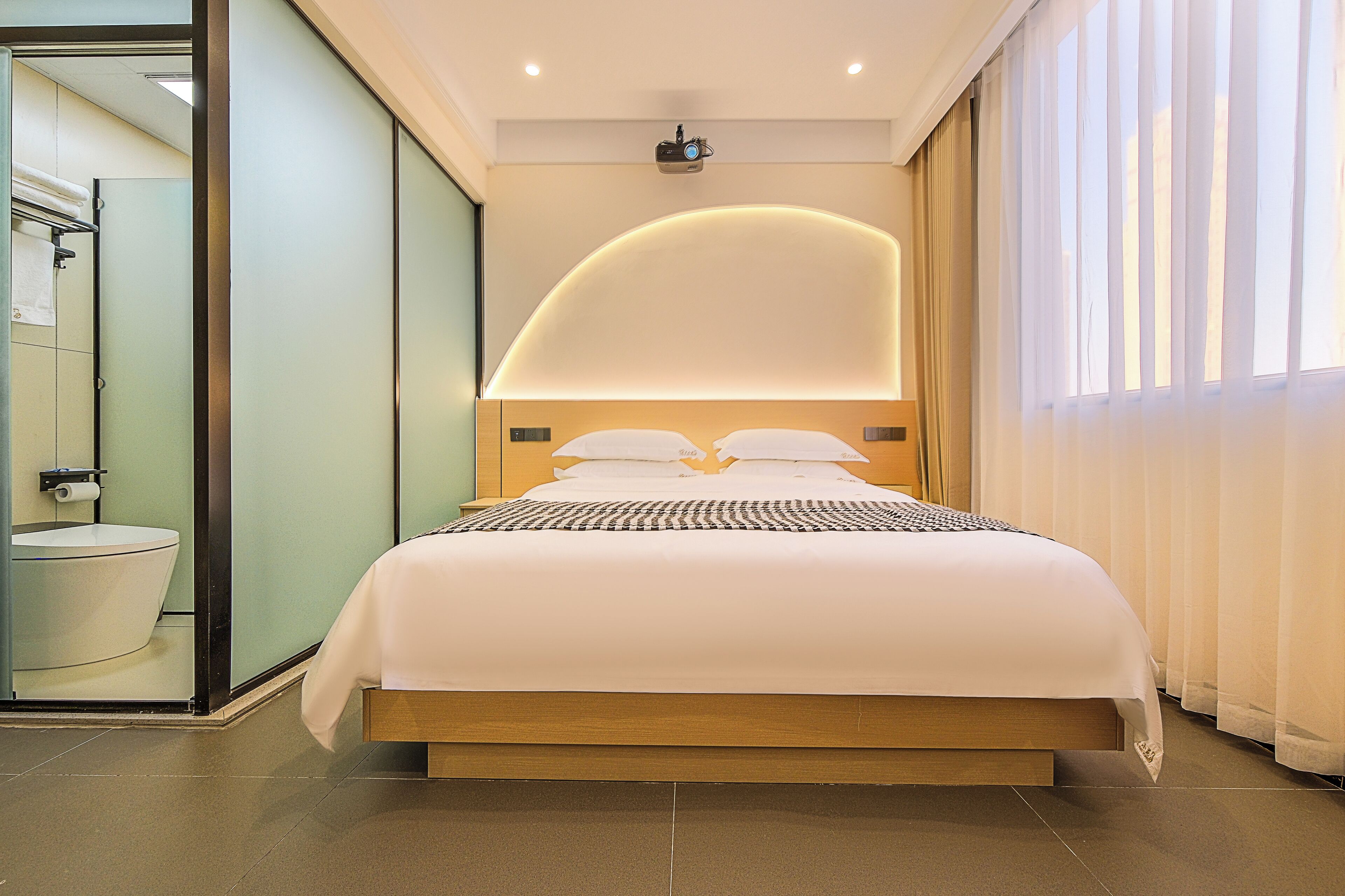 A modern hotel room with a large bed, a built-in shower, and a large window with curtains.