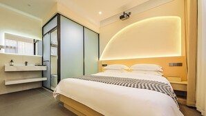 Ein modernes Hotelzimmer mit einem großen Bett, einem eingebauten Kleiderschrank, einem Nachttisch und einem Spiegel.
