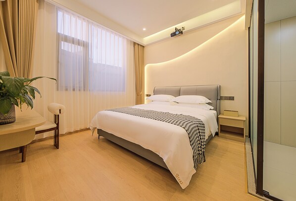 A modern hotel room with a large bed, a bedside table, a chair, and a potted plant.