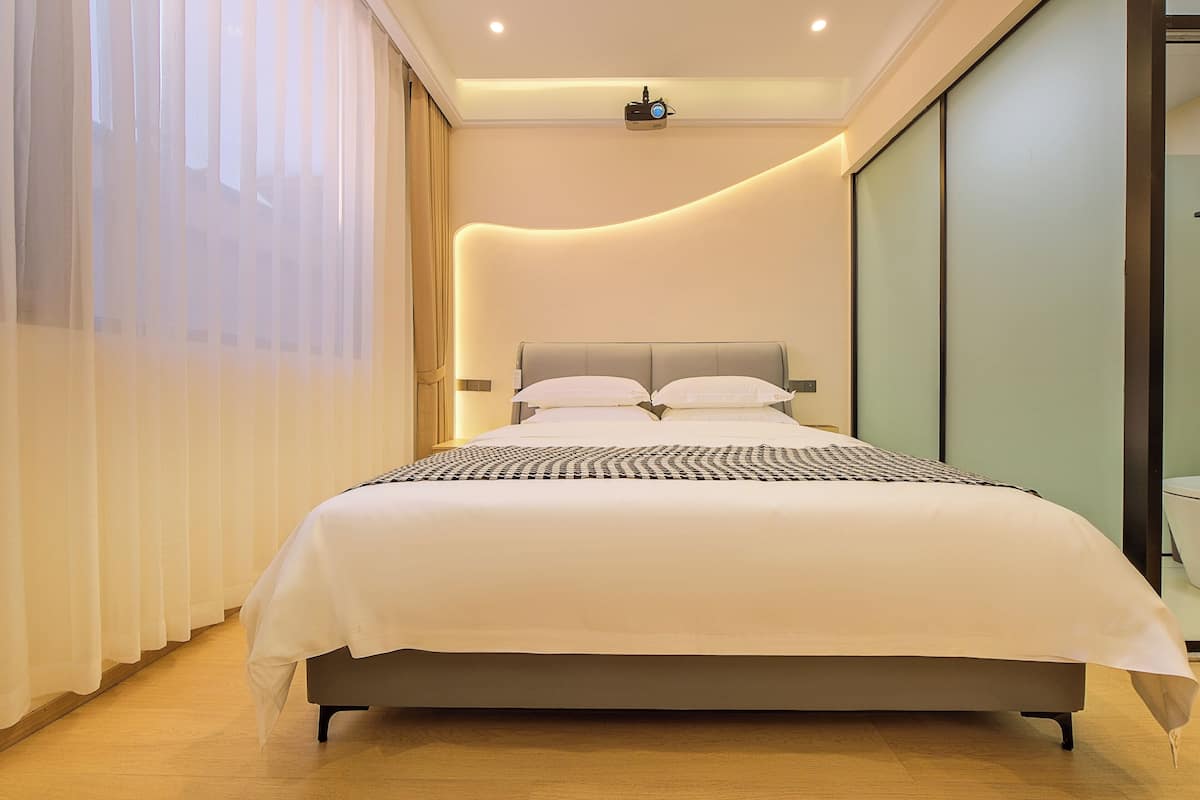 A modern hotel room with a large bed, a projector on the ceiling, and a sliding glass door.