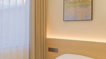 A hotel room with a bed, a painting of a landscape, and a window with curtains.