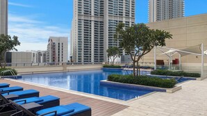 A rooftop pool area with lounge chairs, a clear blue sky, and high-rise buildings in the background. - Elegant 1BR with Panoramic Views (Dubai)