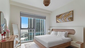 A modern bedroom with a large bed, a bedside table, a nightstand, a mirror, and a window with a city view. - Elegant 1BR with Panoramic Views (Dubai)