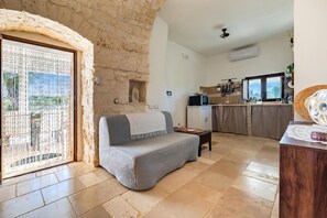 A cozy living area with a sofa, a wooden table, and a kitchen in the background. - Trullo Conosolo With Pool (Martina Franca)