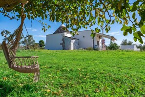 A white building with a conical roof, surrounded by a grassy field and a hammock. - Trullo Conosolo With Pool (Martina Franca)