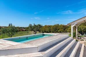 A swimming pool with steps leading to a covered area, surrounded by greenery and trees. - Trullo Conosolo With Pool (Martina Franca)