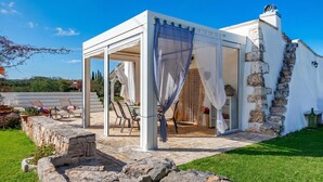 En vit pergola med en täckt uteplats, stentrappor och utsikt över landskapet.