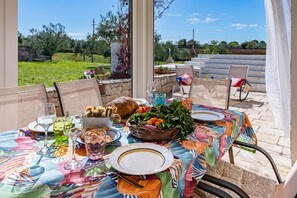 An outdoor dining area with a table set for a meal, surrounded by chairs, and a view of the countryside. - Trullo Conosolo With Pool (Martina Franca)