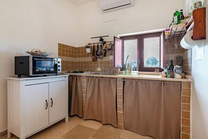 A kitchen with a microwave, cabinets, a window, and various kitchen utensils. - Trullo Conosolo With Pool (Martina Franca)