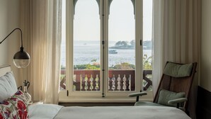 Une chambre avec une grande fenêtre, un lit, une chaise et une lampe.