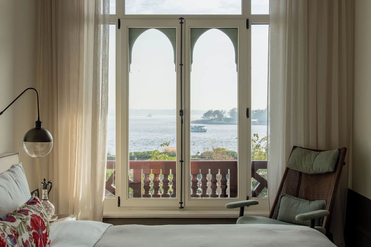 A bedroom with a large window, a bed, a chair, and a lamp.