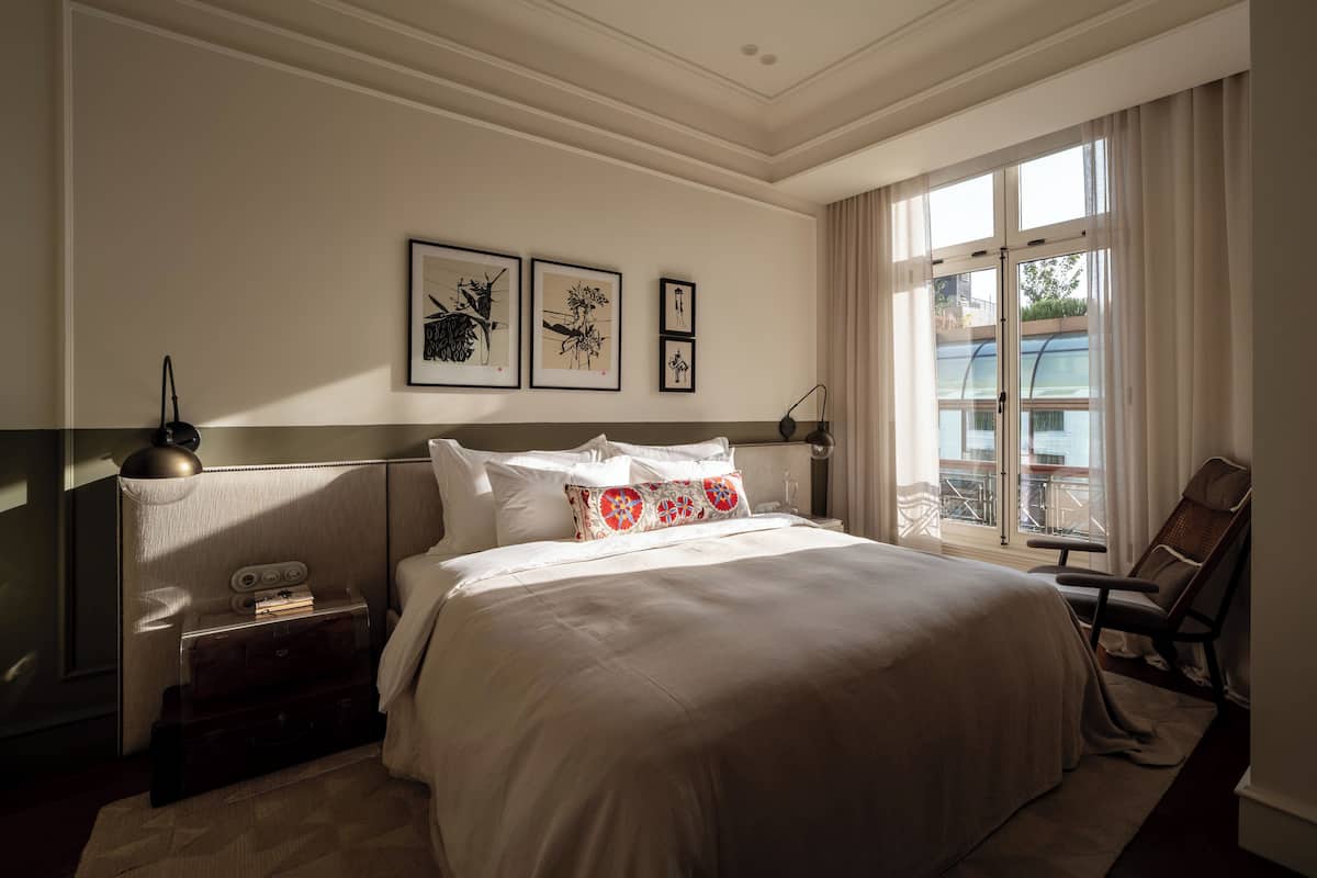 A hotel room with a large bed, a nightstand, a chair, and a window with a view of the outside.