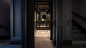 Un couloir avec un comptoir d’accueil aux couleurs sombres, un tableau encadré au mur et un tapis à motifs sur le sol.