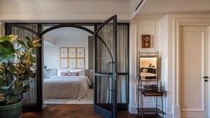 Une chambre d’hôtel avec un lit, une plante en pot, un miroir et une étagère avec quelques objets.